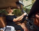 Blonde woman in sunglasses and in black dress sits in old vintage classic car