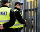 Two policemen stand in front of the entrance gate to the house during home intervention